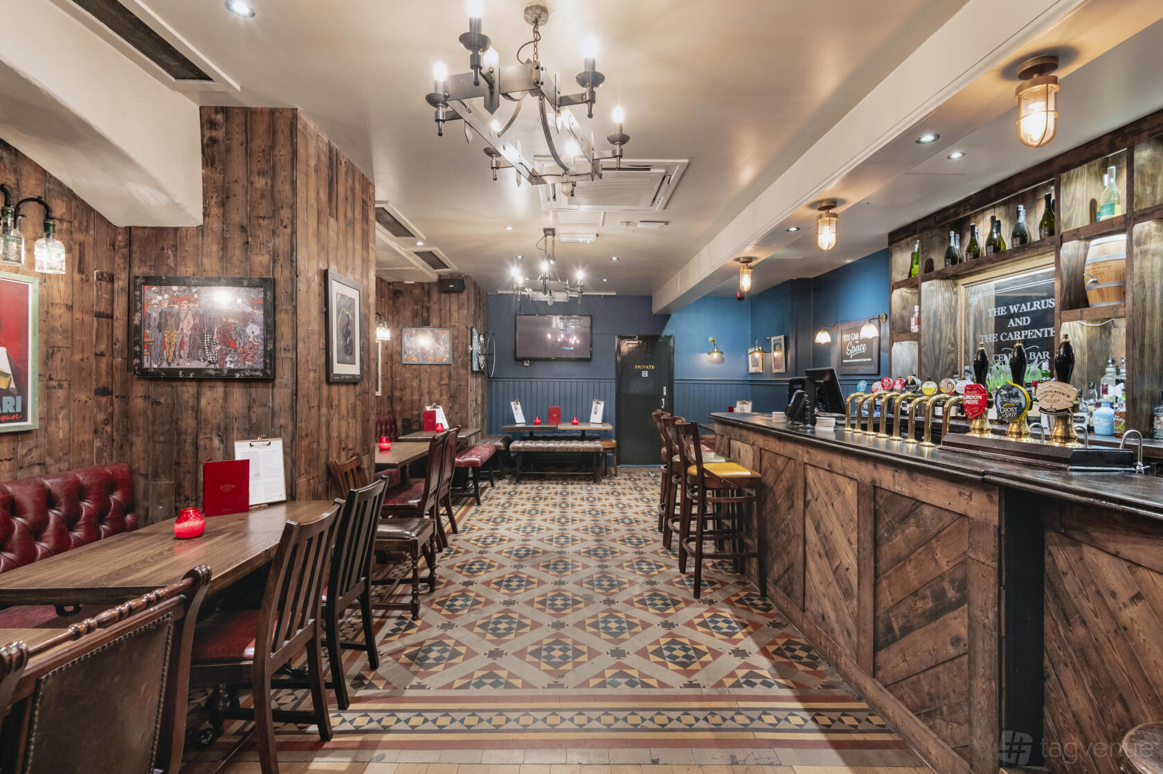 A pub with patterned tile flooring, wooden paneled walls, leather seating, and a long bar at The Walrus and Carpenter.