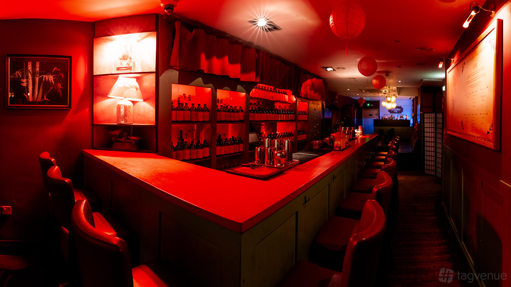 An event space with red lighting, high-backed chairs, and shelves of bottles behind the bar at Opium Cocktail & Dim Sum Parlour.