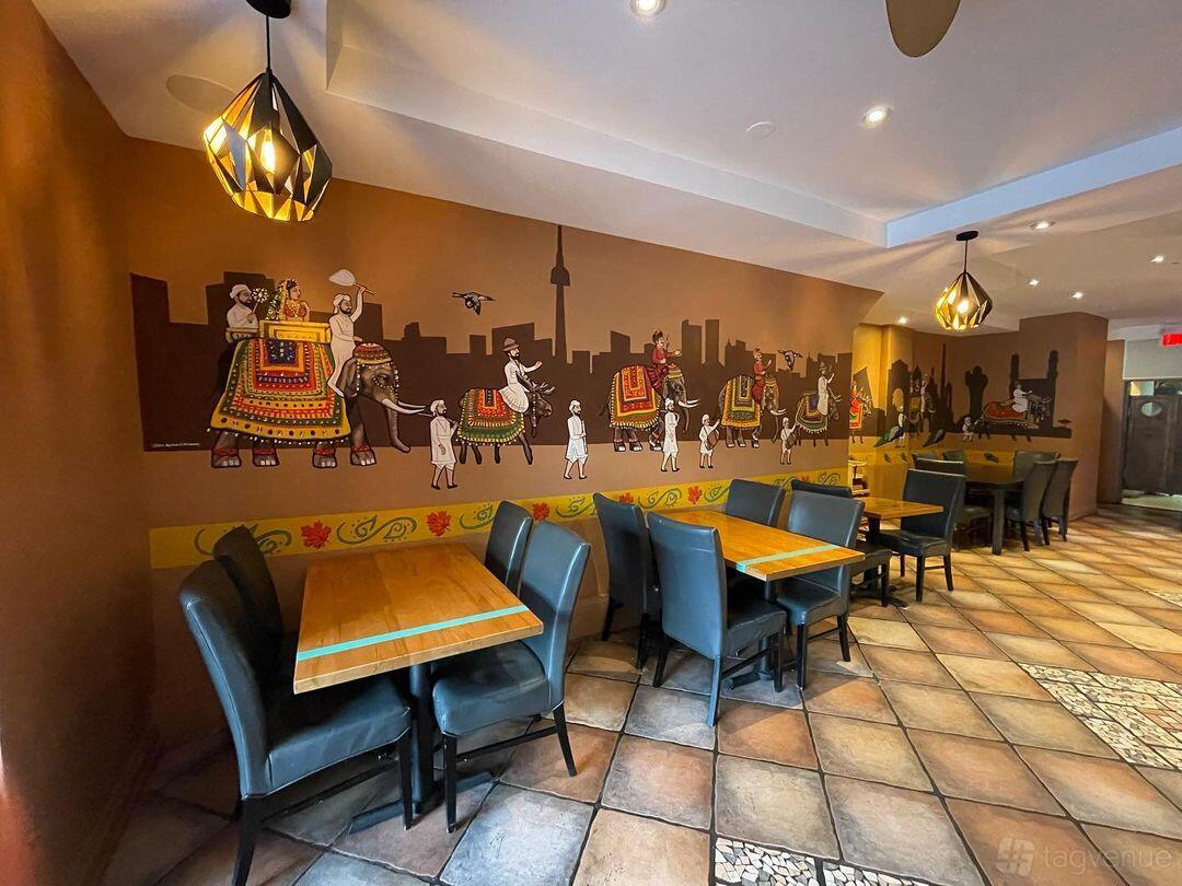 A restaurant with mural art of elephants and cityscape, wooden tables, and black leather chairs at Koshaa Fine Indian Cuisine.