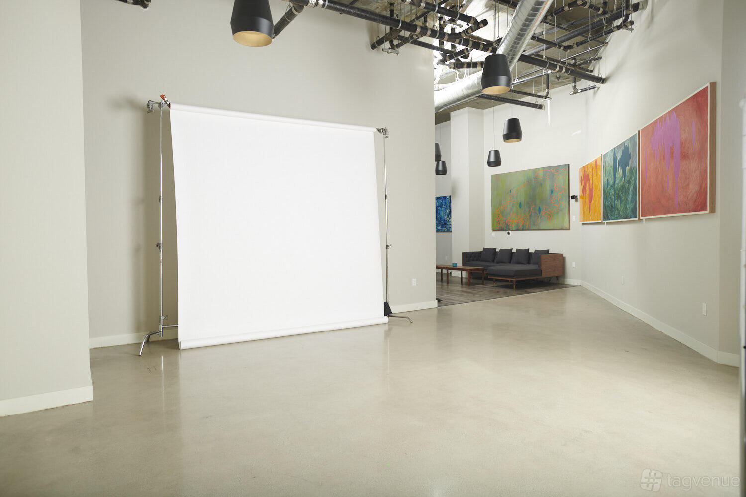 A photo studio with a large white backdrop, exposed ductwork, and colorful abstract art at Verge Studios.