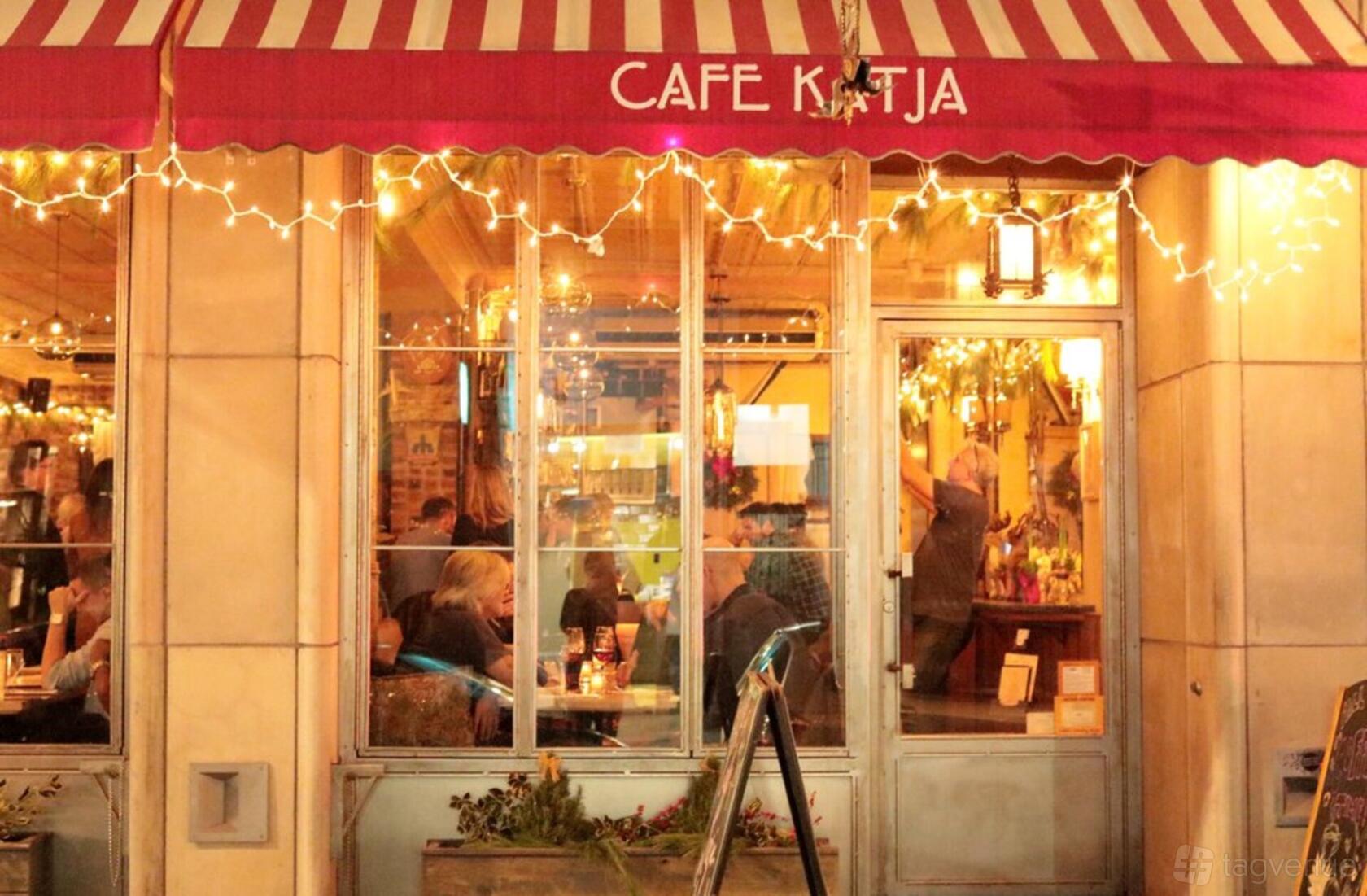 A restaurant with a red striped awning, large windows, and string lights at Cafe Katja.