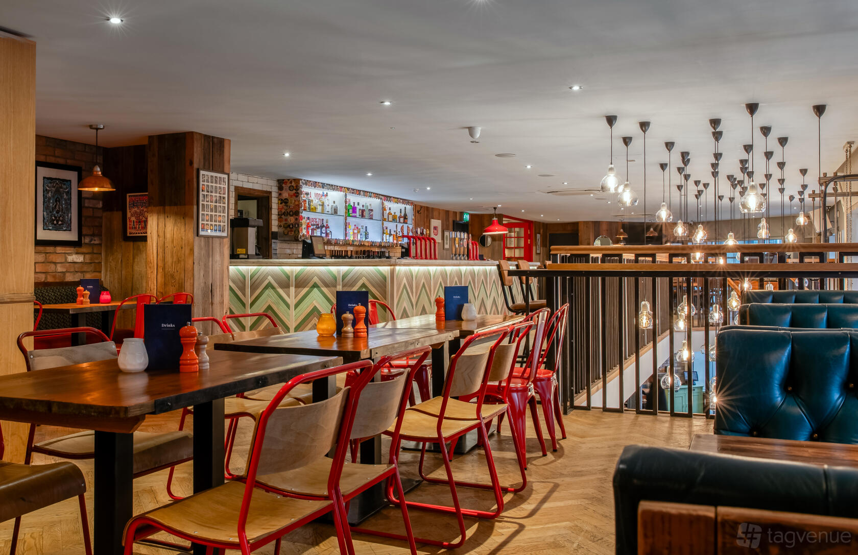 An event space in a pub with wooden tables, red metal chairs, and hanging pendant lights at The Hydrant.
