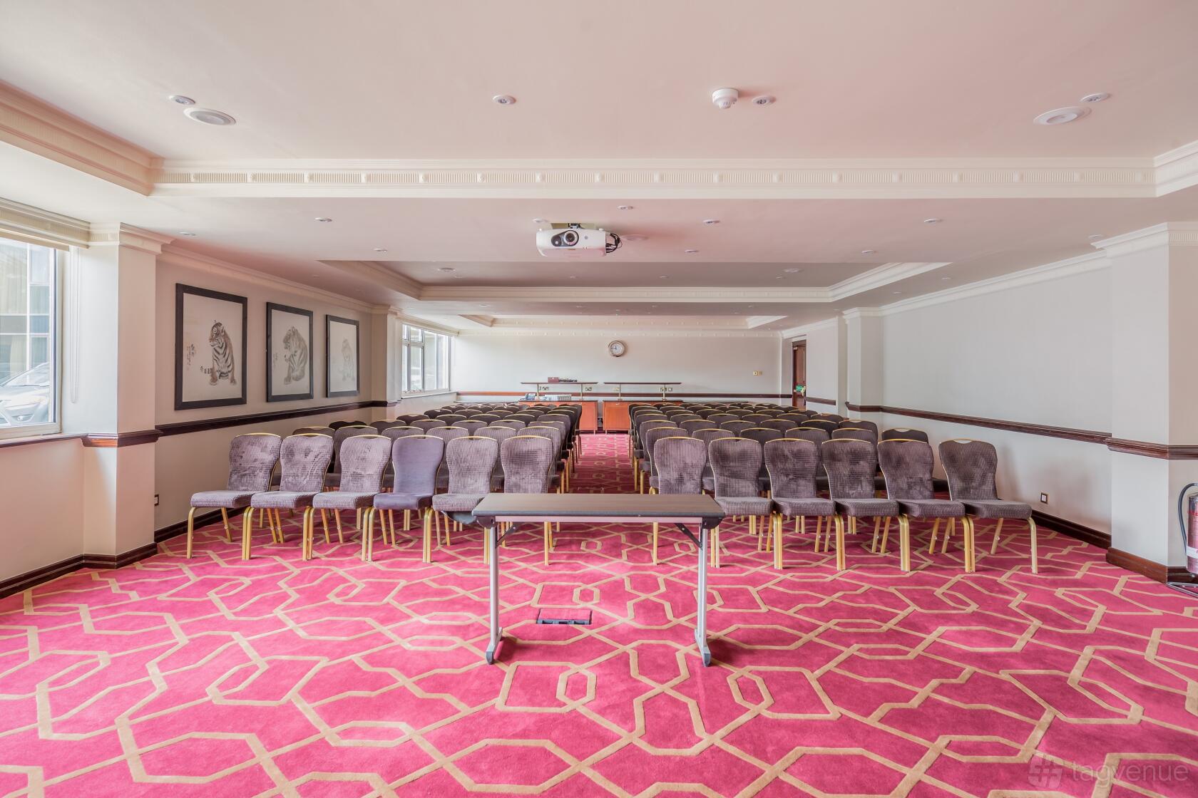 An auditorium with rows of cushioned chairs, projector, and large windows at Radisson Blu Hotel, London Heathrow.