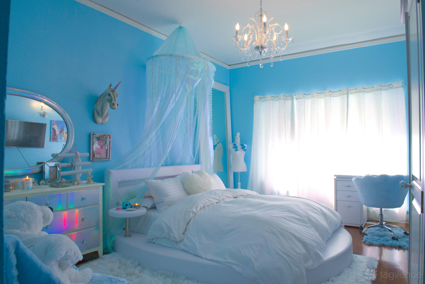 An event venue room with pastel blue walls, a white bed under a canopy, chandelier, and natural light at Sparkl Palace.