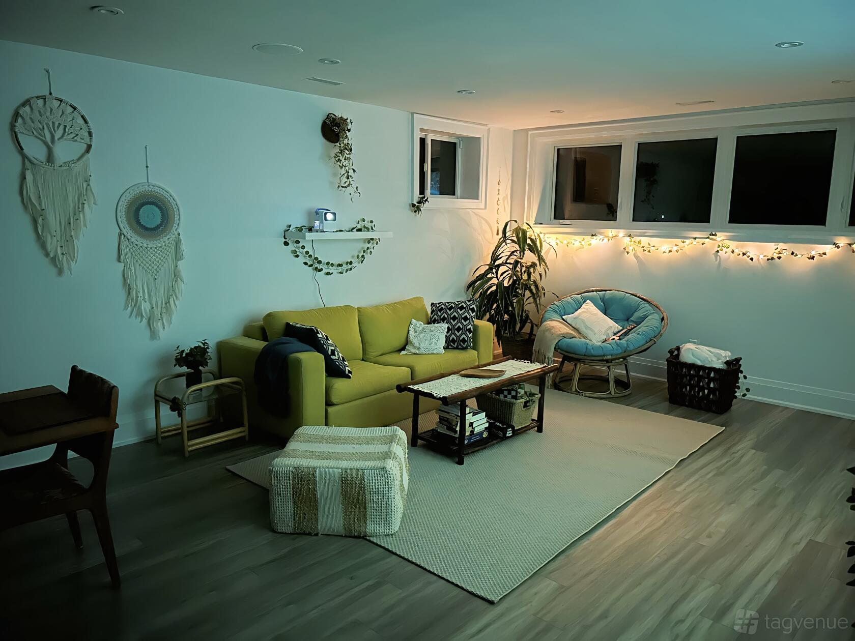 A cozy basement apartment with a yellow sofa, macrame wall hangings, string lights, and light wood floors at The Adair Bellmont.
