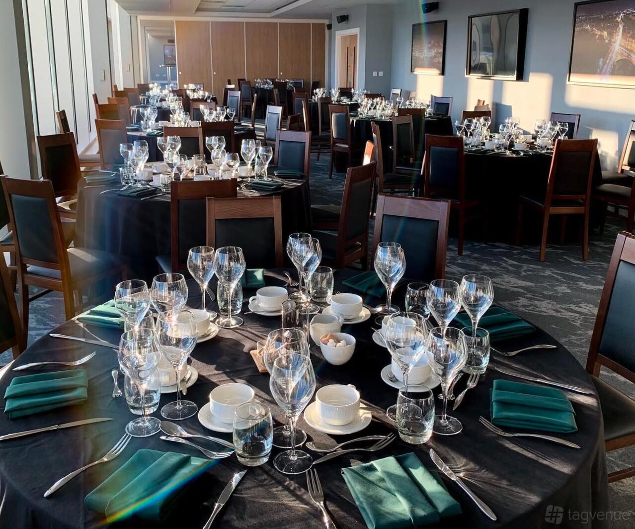 A hotel lounge with round tables set with glassware, white china, and dark green napkins at Tynecastle Park.