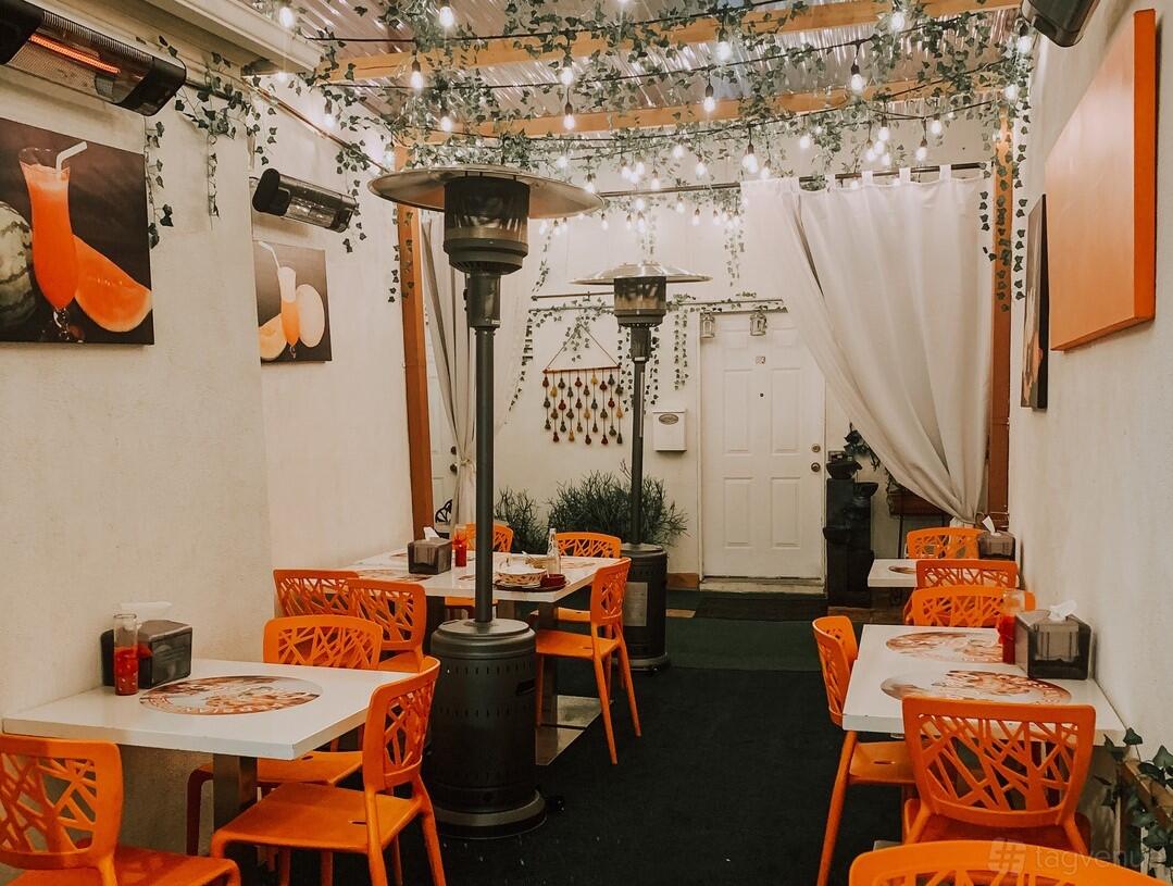 A restaurant with orange chairs, white tables, patio heaters, string lights, and wall art at Cafe Glace.