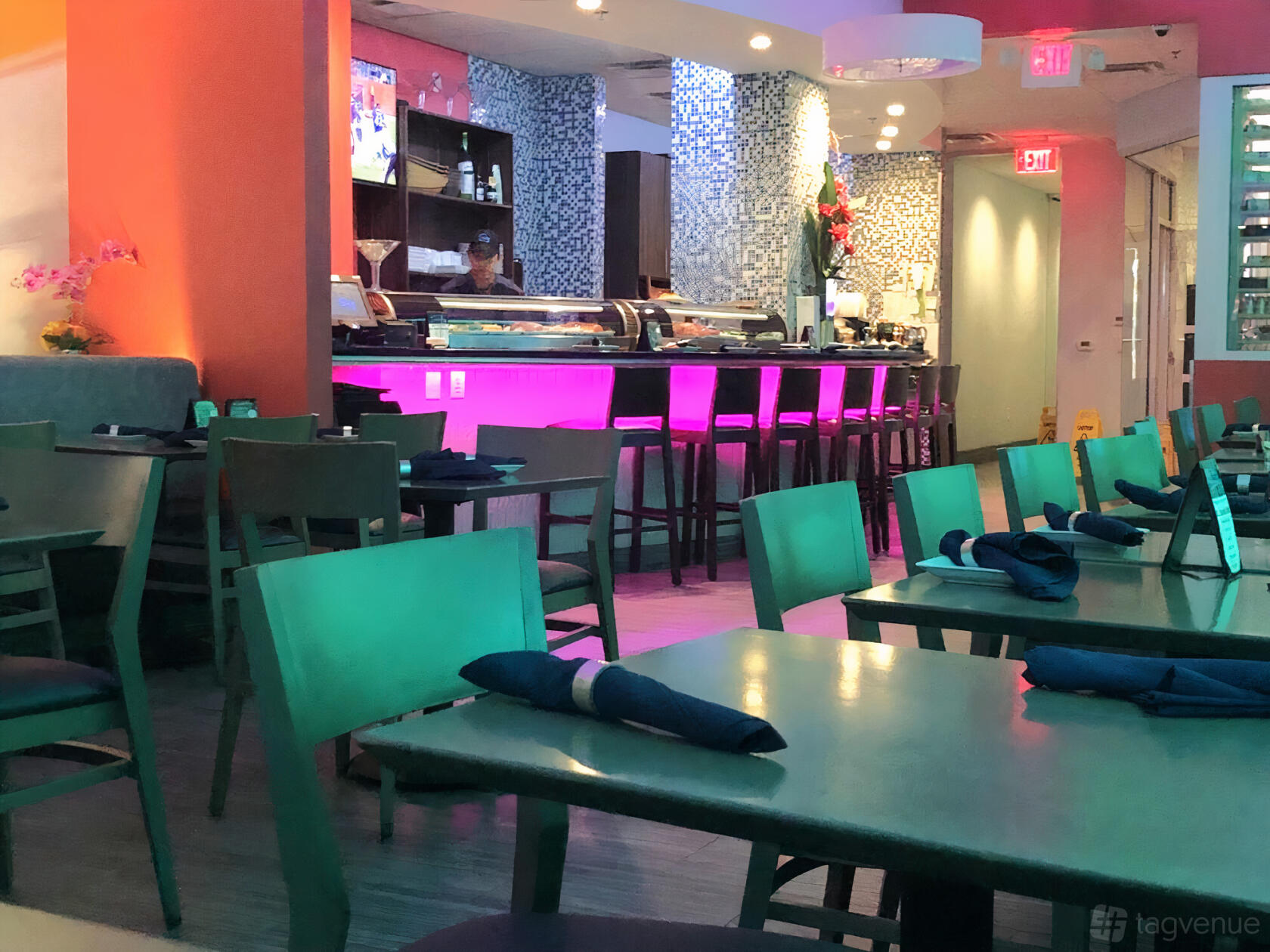 A restaurant with green tables, wooden chairs, and a sushi bar lit by purple lights at Sky Thai Sushi.