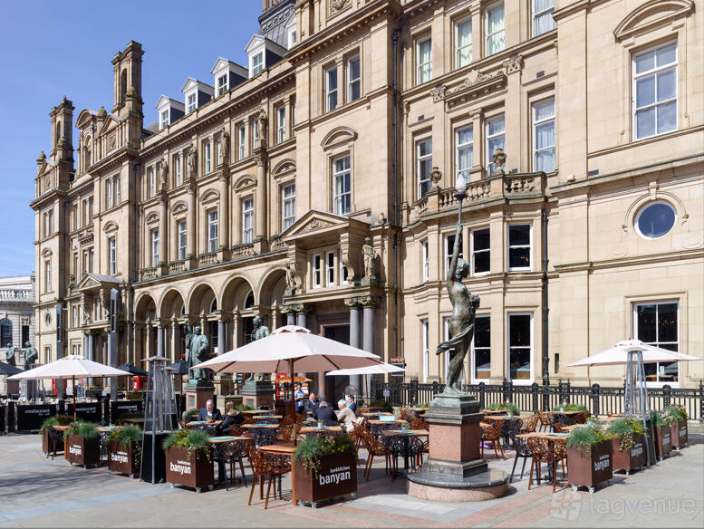 A restaurant with outdoor seating, large umbrellas, and planters in front of a historic stone building at Banyan Bar & Kitchen.