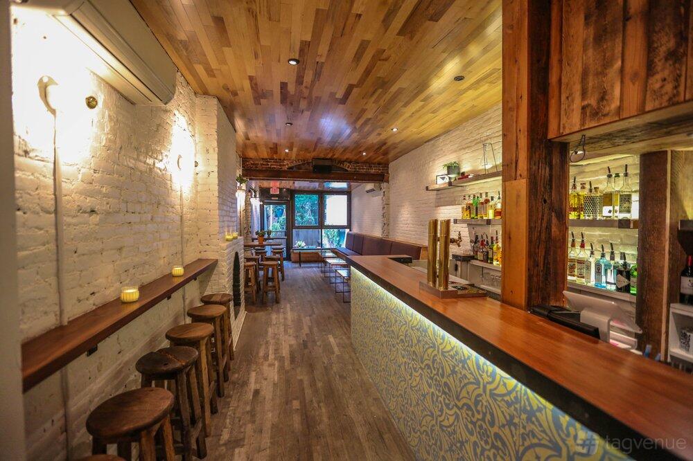An event space in a bar with a patterned counter, wooden stools, exposed brick walls, and a wood-plank ceiling at Hidden Lane Bar.