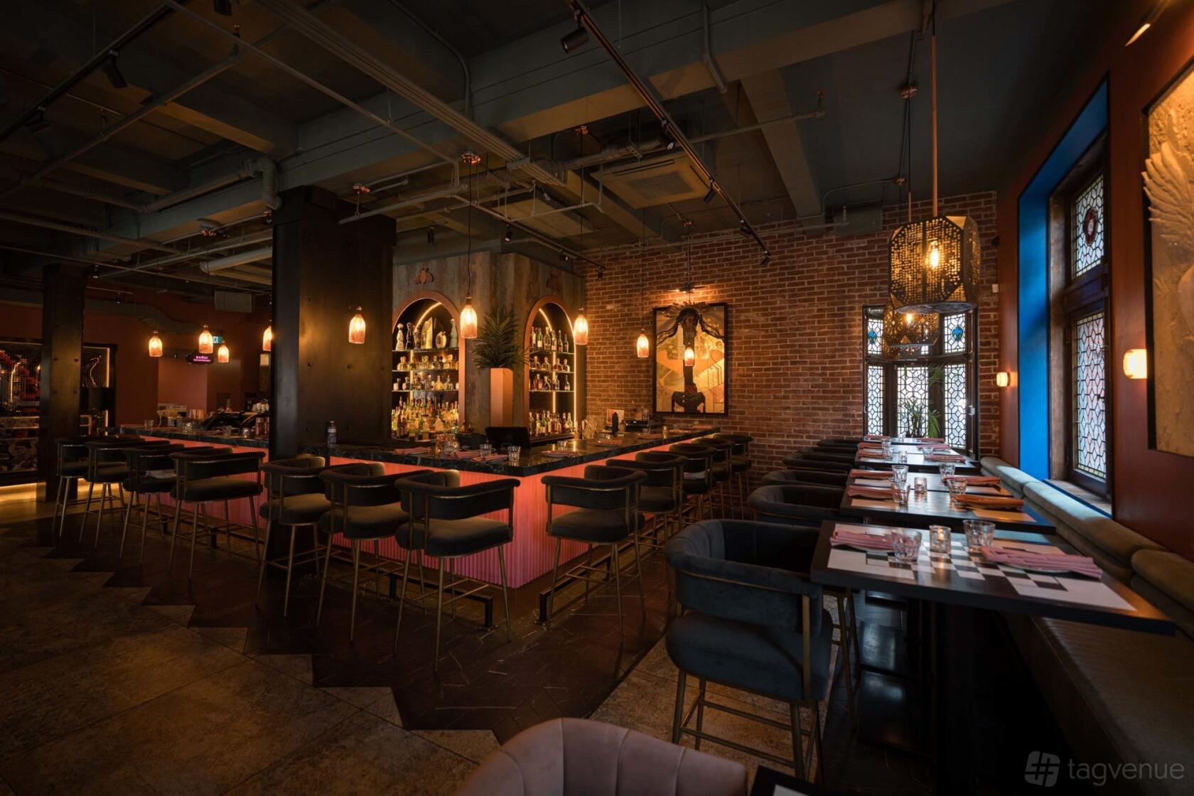 A dining room with exposed brick walls, pendant lighting, and a central pink bar with high chairs at Silent H.