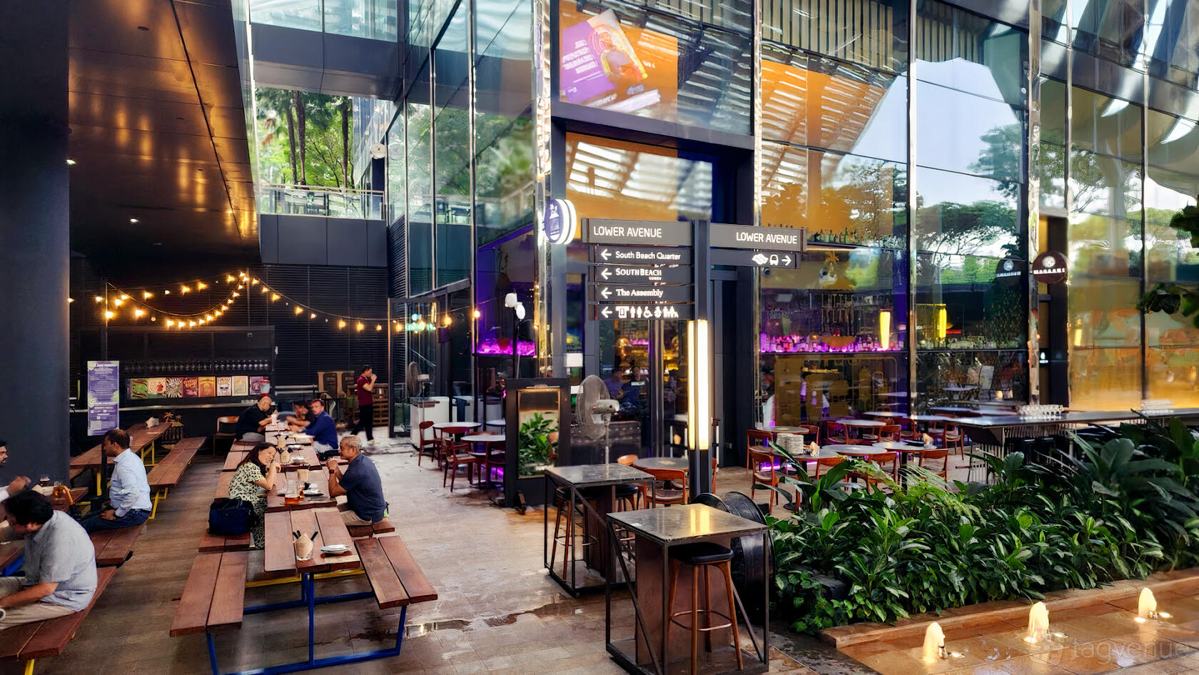 An open-air bar courtyard with long wooden tables, string lights, and lush greenery at Little Island Brewing Co. - South Beach.