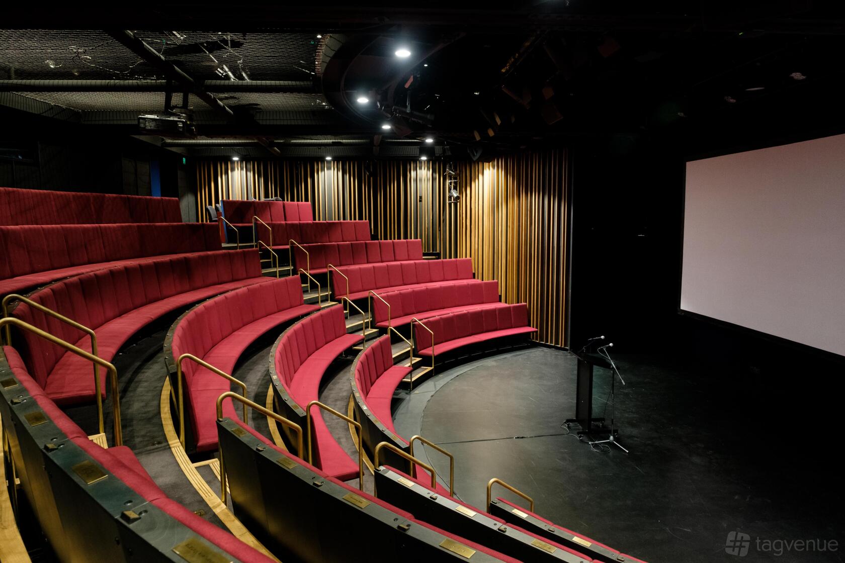 A theatre with curved tiered seating, red upholstered chairs, and a large projection screen at Australian Theatre for Young People.