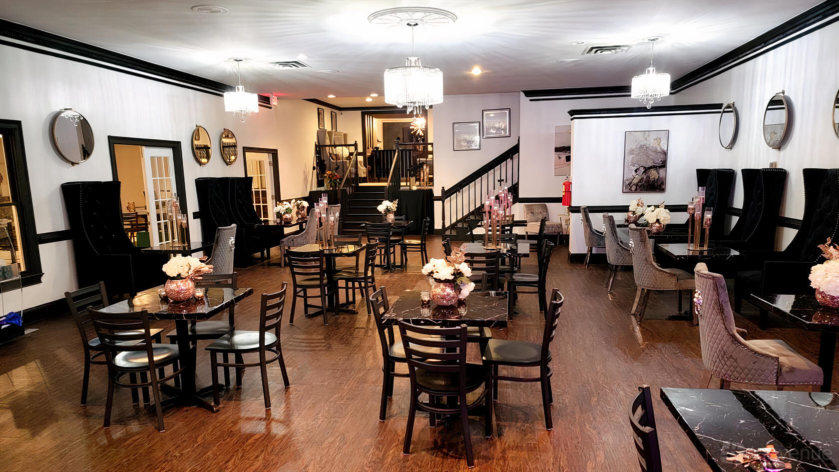 A ballroom with dark wood floors, marble tables, floral centerpieces, and chandeliers at The Garden's Executive Club.