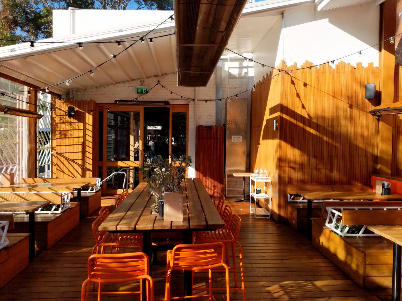 An outdoor dining area with wooden picnic tables, orange chairs, and string lights at Fonda Mexican @ Hawthorn.