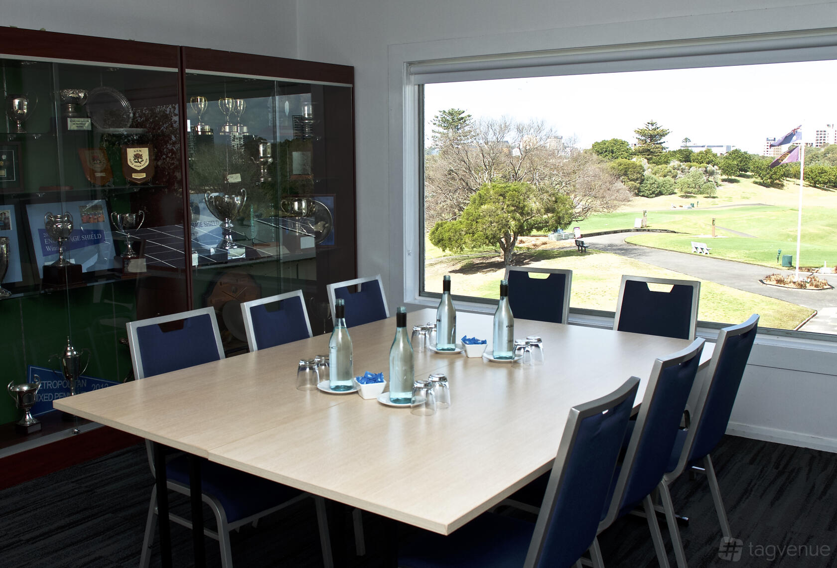 A meeting room with a large window overlooking the golf course, a rectangular table, and trophy display at Moore Park Golf Club.