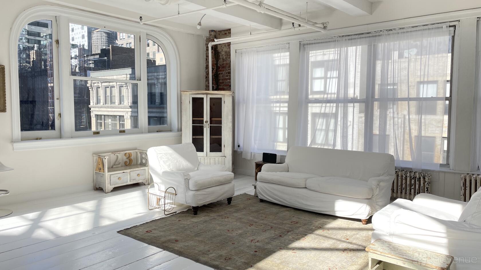A loft with large arched windows, sheer curtains, white furnishings, and exposed brick at Gary's Loft.
