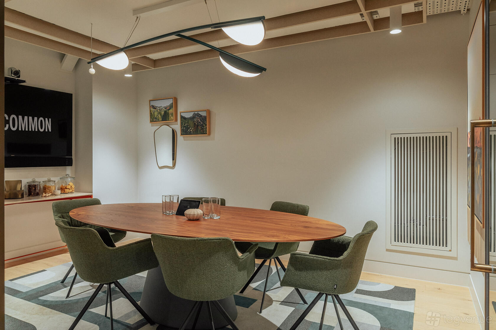 A meeting room with an oval wooden table, six green chairs, and modern ceiling lights at Uncommon Holborn.