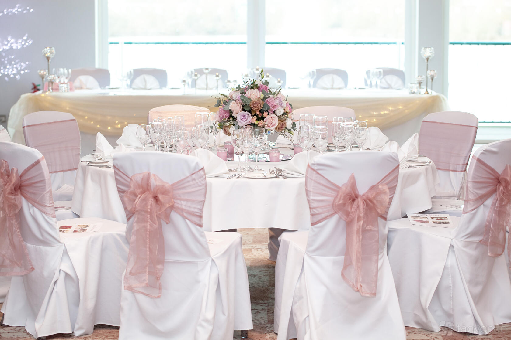 An auditorium with round tables covered in white linens and pink sash chairs at Crowne Plaza Marlow Winterlake Suite.