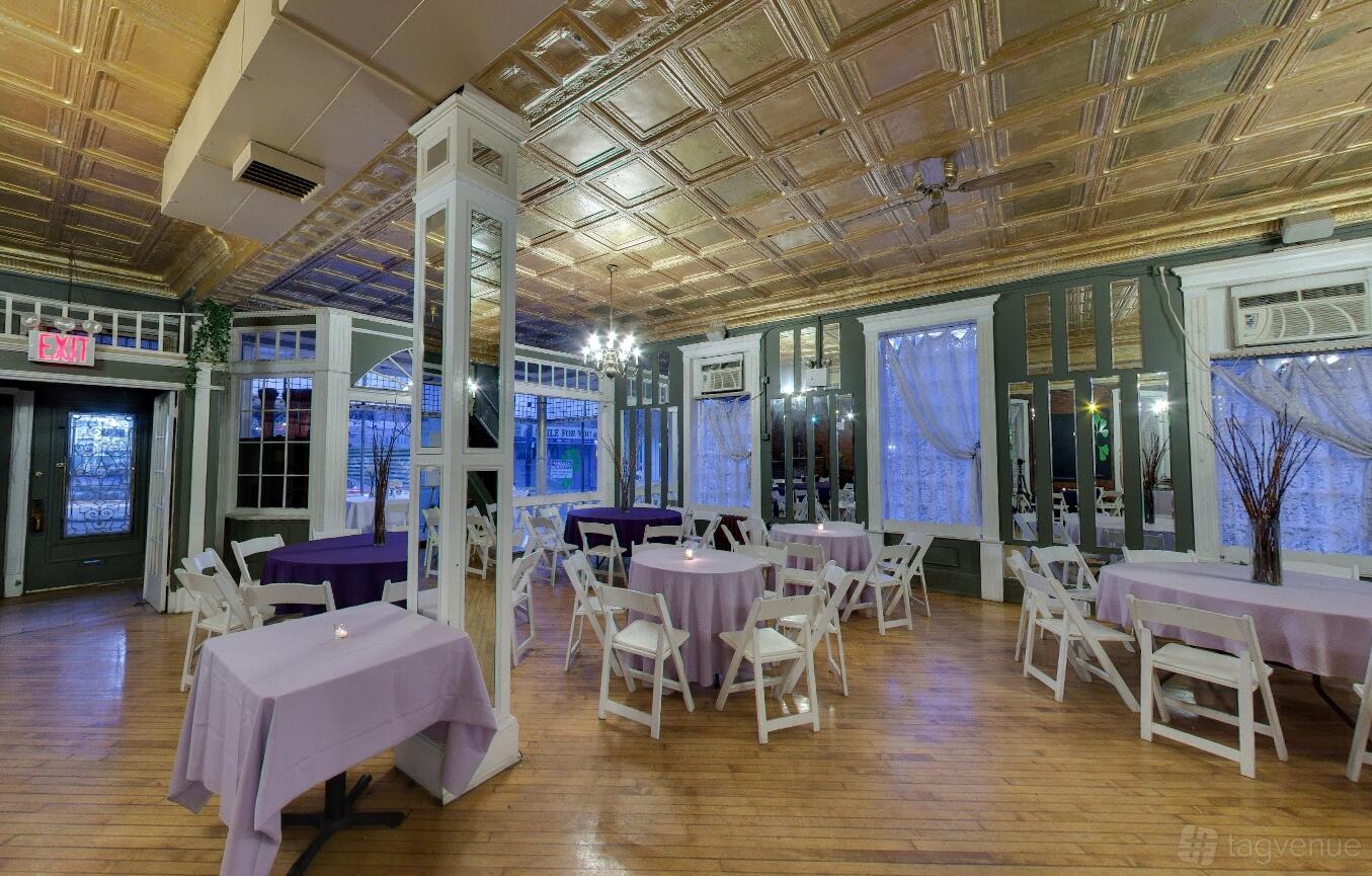 A hall with gold coffered ceiling, wood floors, and round tables with lavender linens at Edgewater Hall.