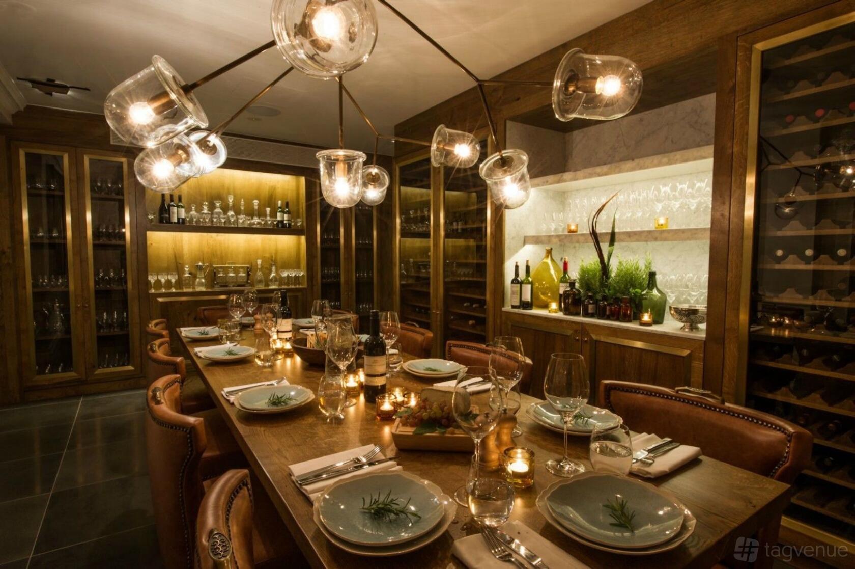 A dining room with a long wooden table, leather chairs, glass pendant lights, and wine displays at The Ampersand Hotel.