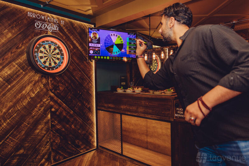 A pub with a wooden dartboard area, electronic scoring screen, and ambient lighting at Arrowsmiths @ O'Neill's Solihull.