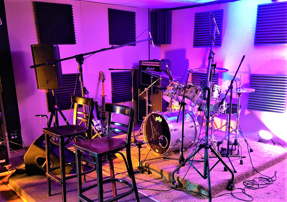 A recording studio with drum kit, amplifiers, guitars, and acoustic foam panels at 1POINT5 Entertainment.