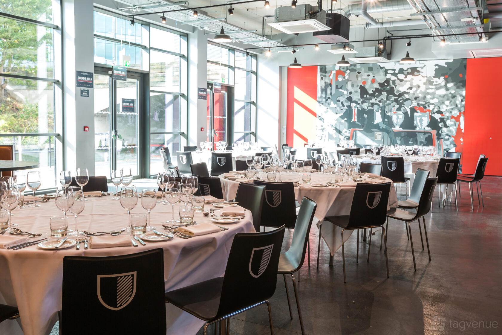 An event space in a hotel with round tables set with glassware, black chairs, and floor-to-ceiling windows at Hotel Football.