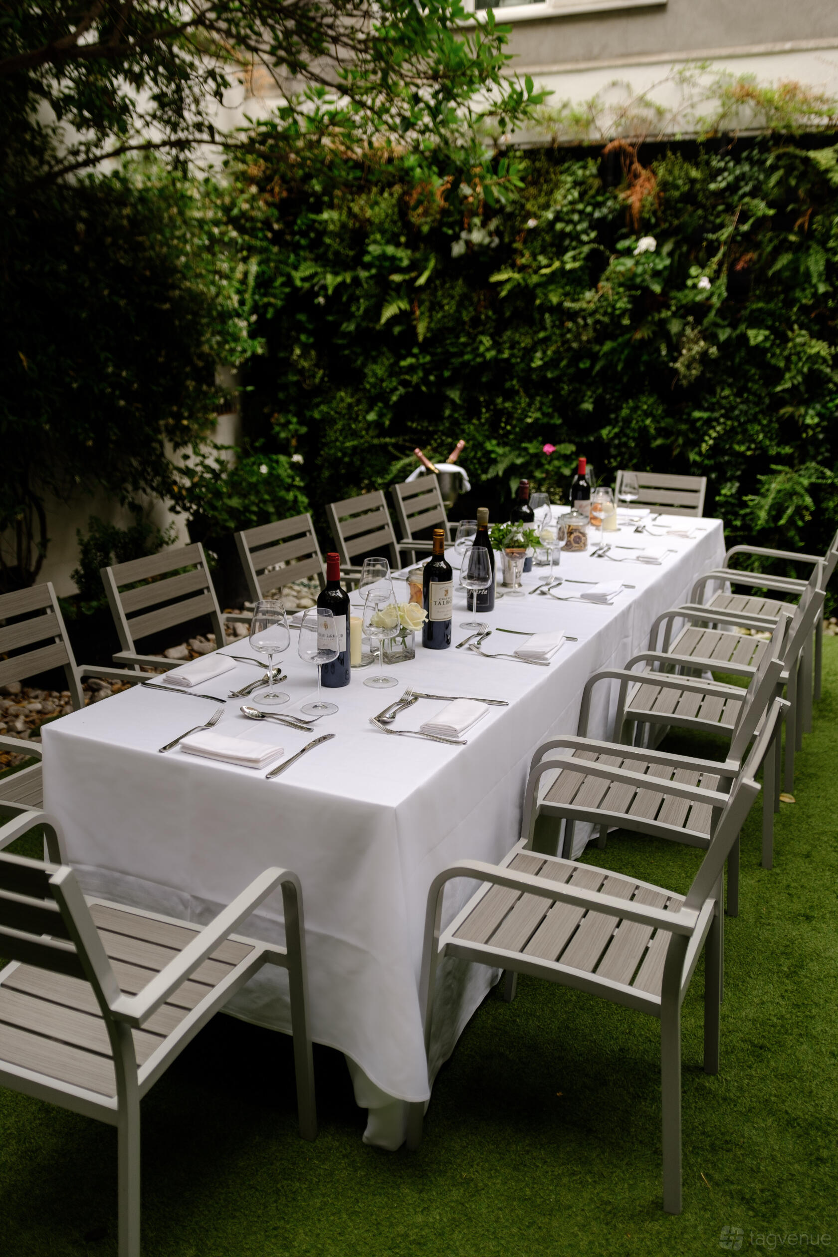 An outdoor dining area with a long table covered in white linens, wine bottles, and modern chairs at The Hyde Restaurant & Bar.