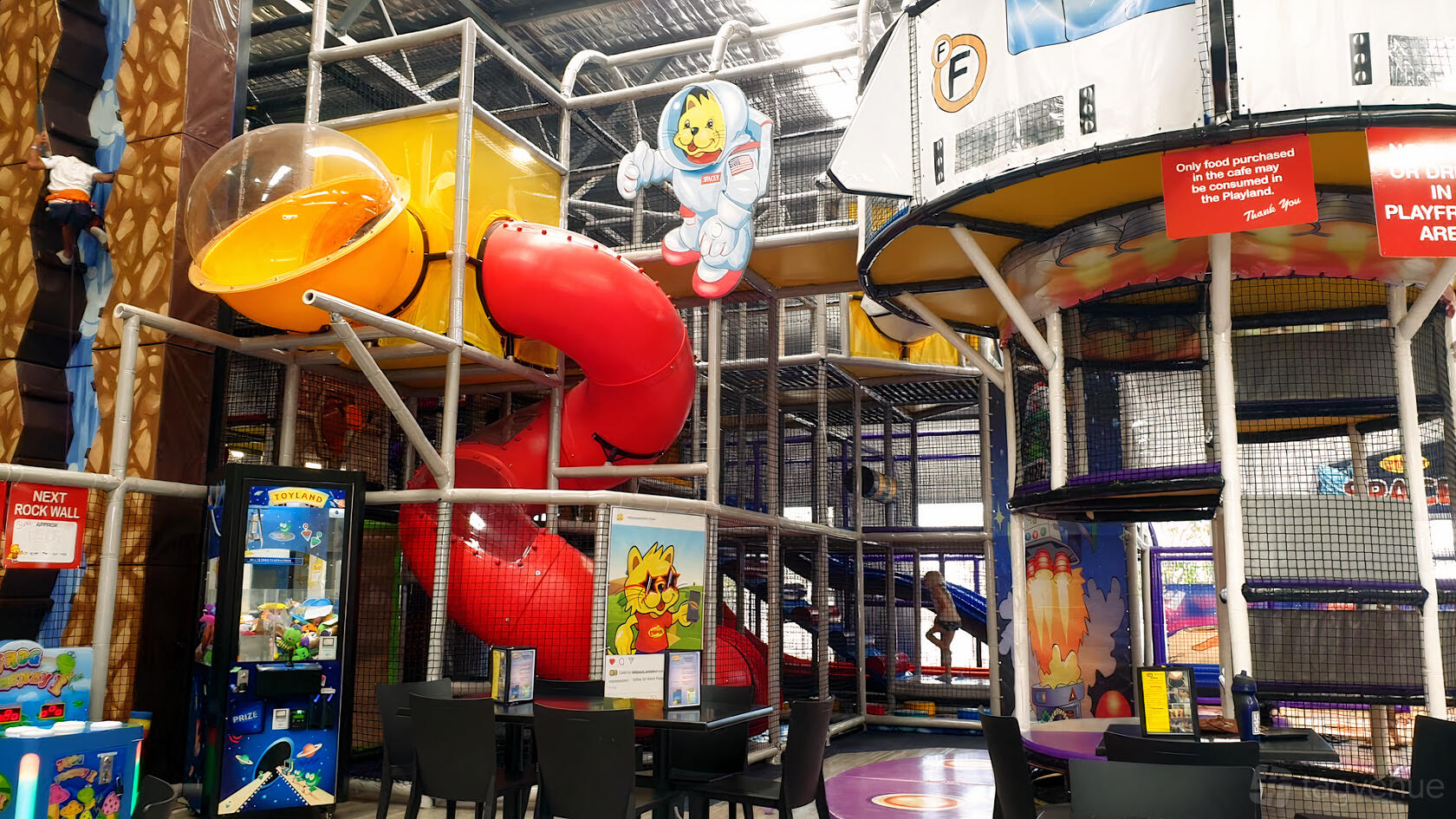 A cafe with colorful indoor playground, red tube slide, climbing structures, and seating at Lollipop's Playland & Cafe Butler.