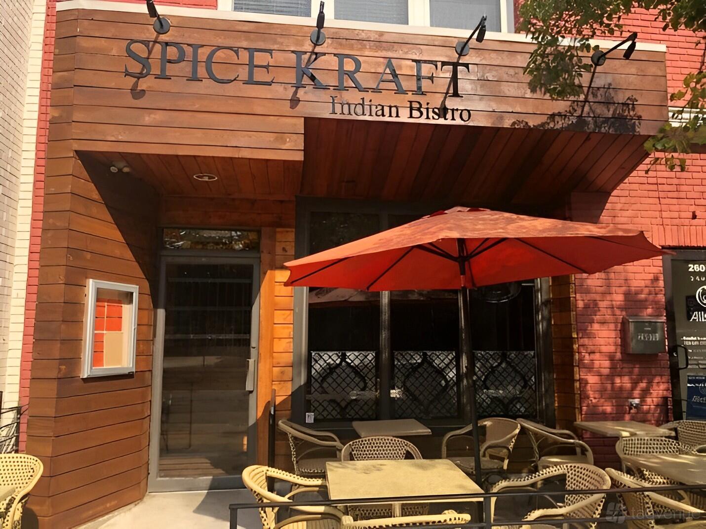 A restaurant with outdoor patio seating, wicker chairs, and a red umbrella at Spice Kraft Indian Bistro Alexandria.
