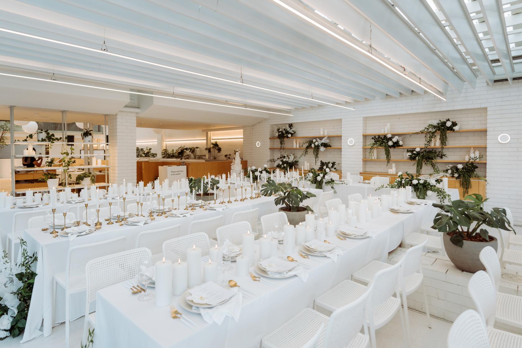 An event space in a cafe with white brick walls, long banquet tables, and greenery at Industry Beans Newstead.