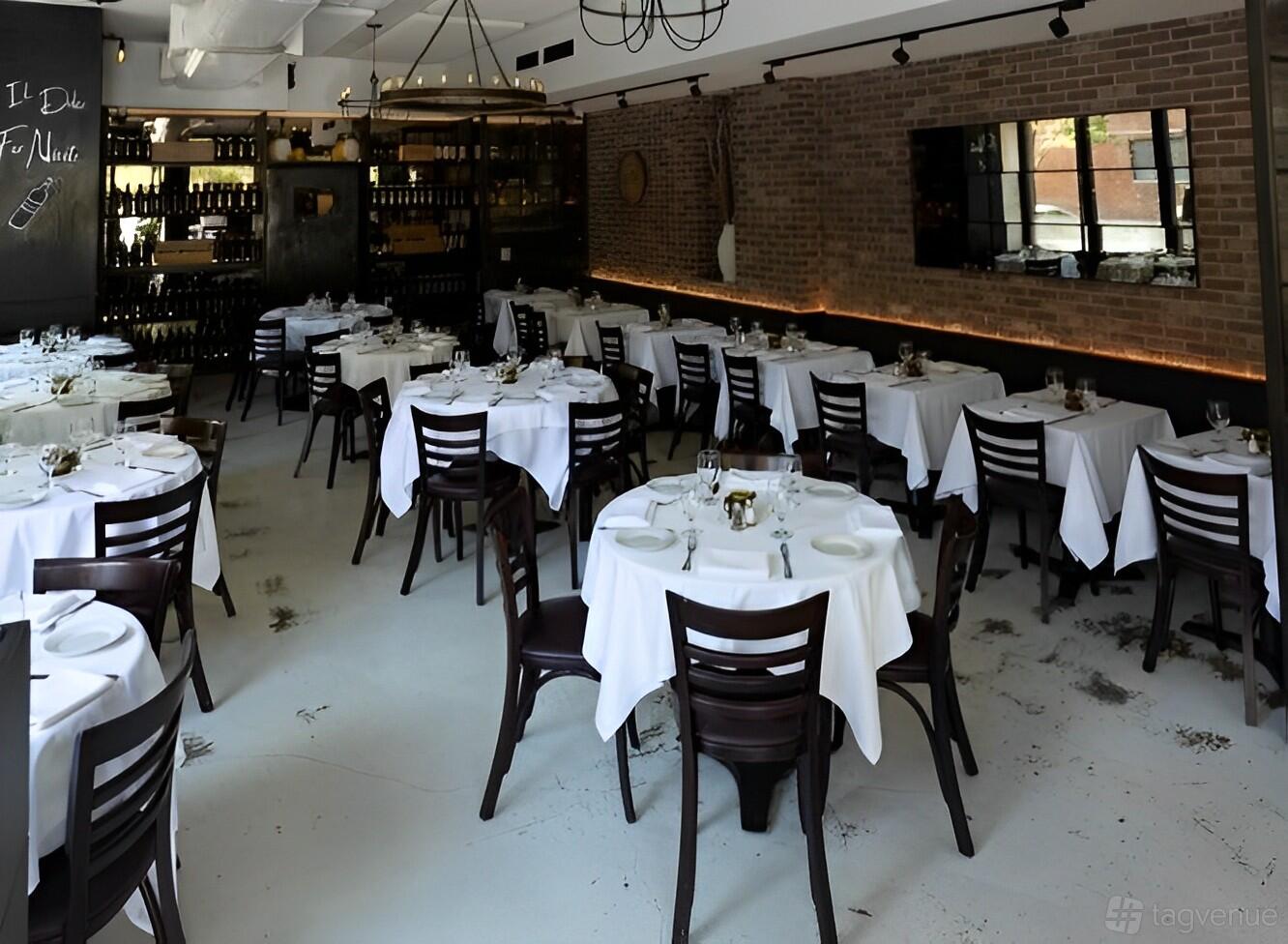 A restaurant dining area with round tables covered in white linens, dark wooden chairs, and exposed brick walls at Osteria Nonnino.