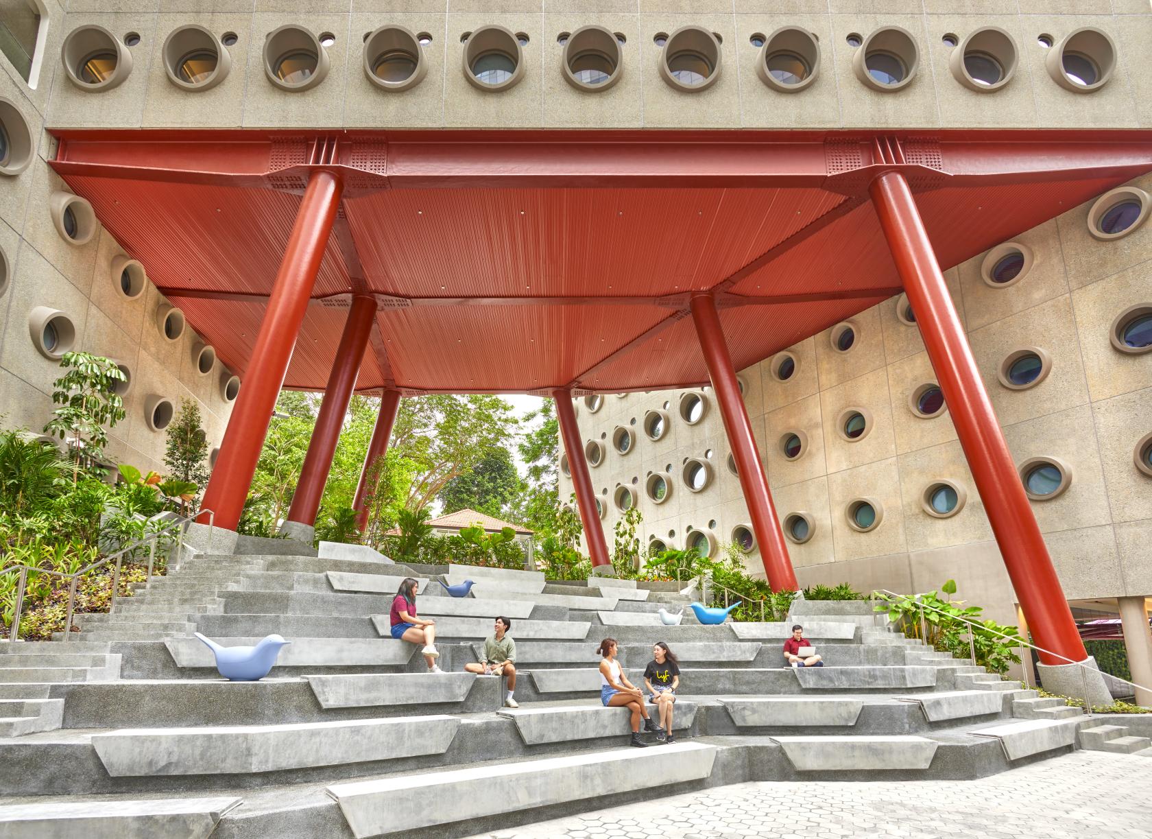 An outdoor amphitheatre with tiered concrete seating and bold red columns at lyf one-north Singapore.