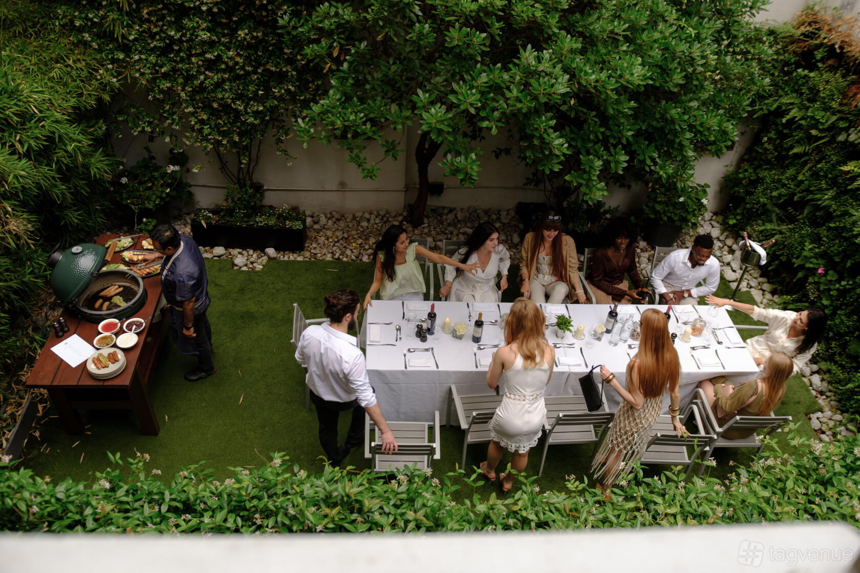 A restaurant garden with a long dining table, white chairs, and lush greenery at The Hyde Restaurant & Bar.