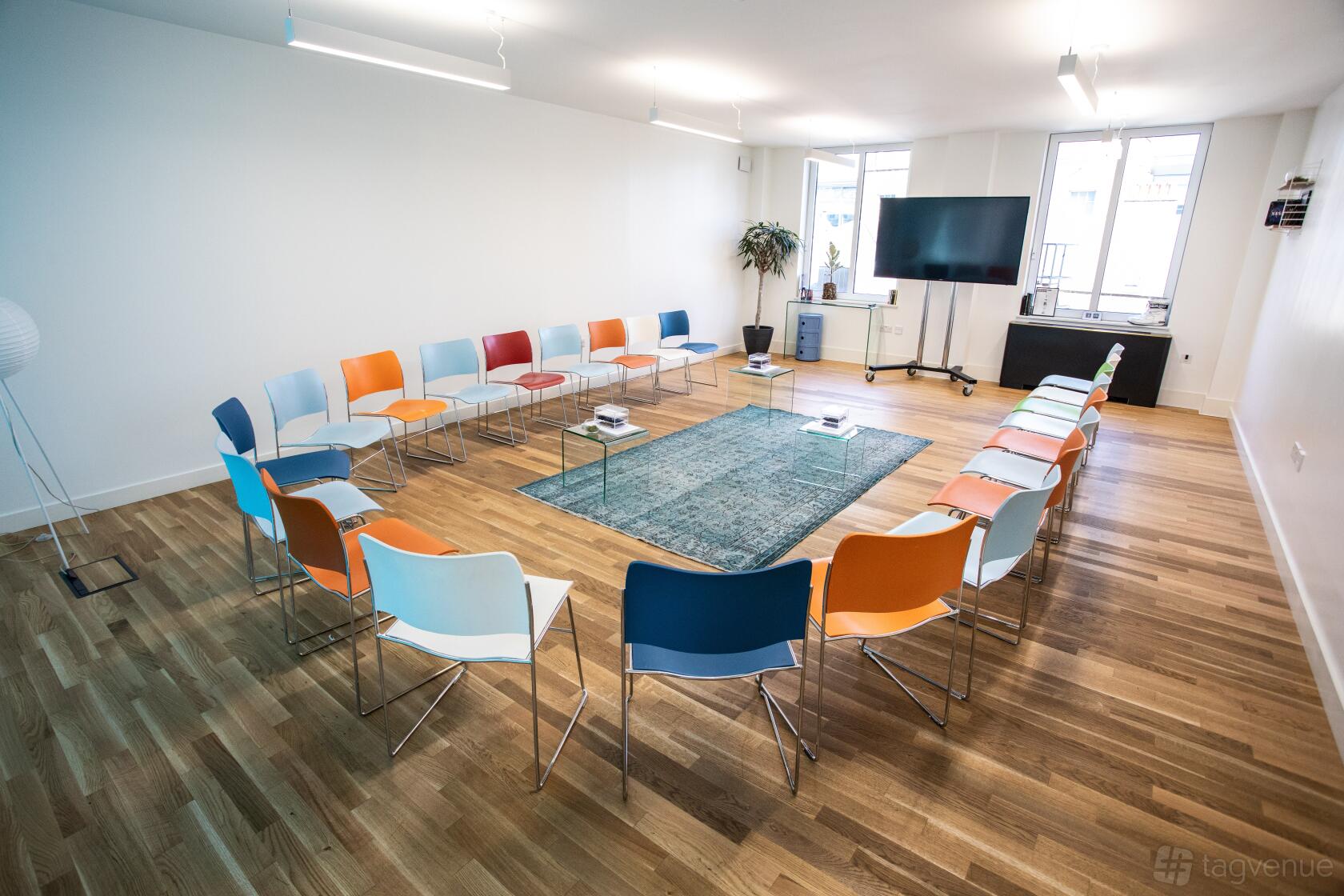 A meeting room with colorful chairs arranged in a circle, a large screen, and natural light at Wallacespace Spitalfields.