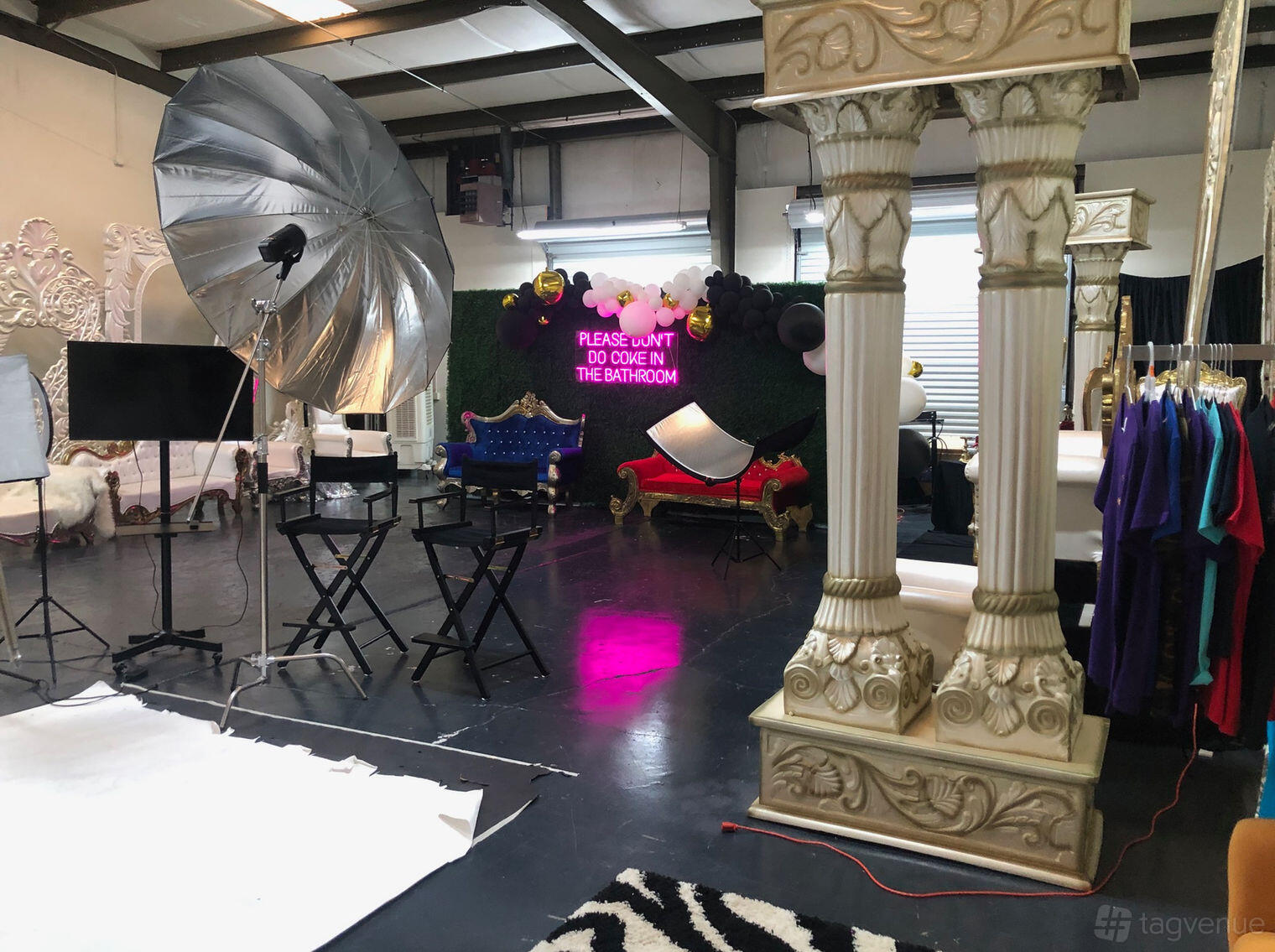 A photo studio with ornate chairs, large softbox lighting, backdrops, and a neon sign at VCAtlanta Photography Studios.