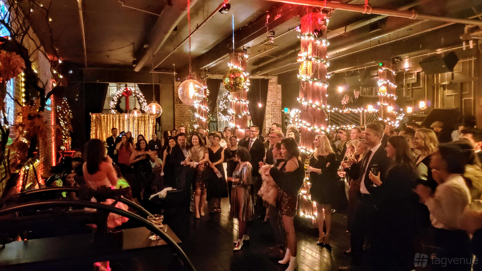 A cocktail bar with exposed brick walls, hanging disco balls, and string lights wrapped around columns at Alchemist Bar & Lounge.