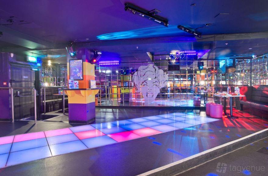 A nightclub with a multicolored light-up dance floor, mirrored walls, and neon lighting at Popworld Watling Street.
