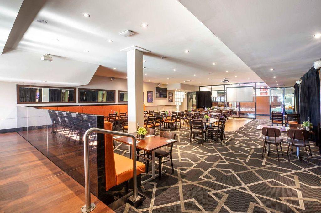 A pub dining area with patterned carpet, wooden tables and chairs, and large windows at Mitcham Hotel.