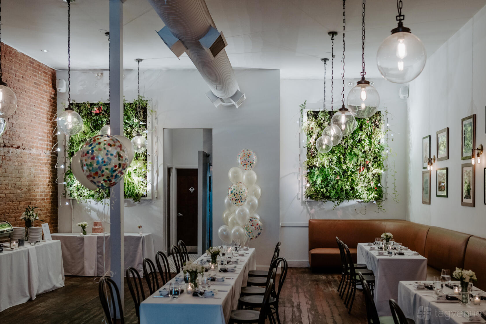 A function room with exposed brick walls, greenery-filled wall decor, and long banquet tables at Gran Morsi.