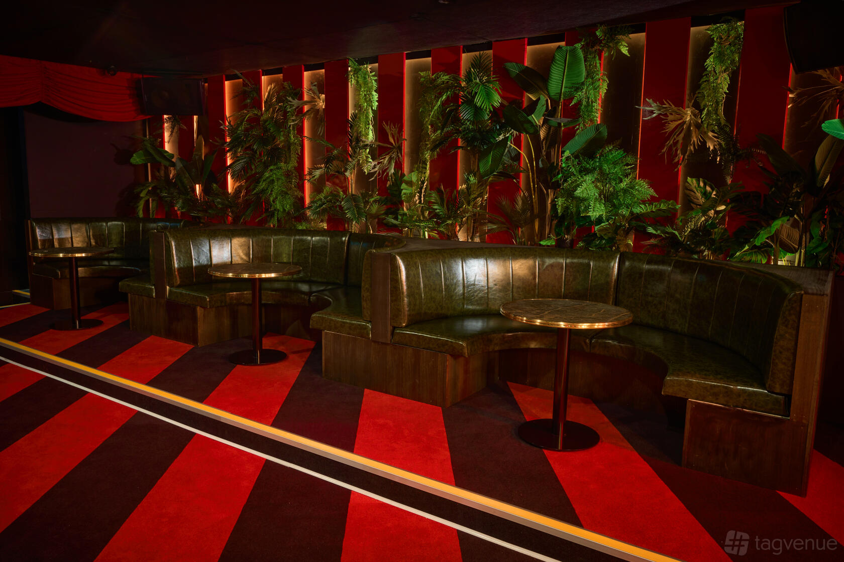 A nightclub lounge with curved green leather banquettes, round tables, and lush plant wall at Carousel Bar & Ballroom.