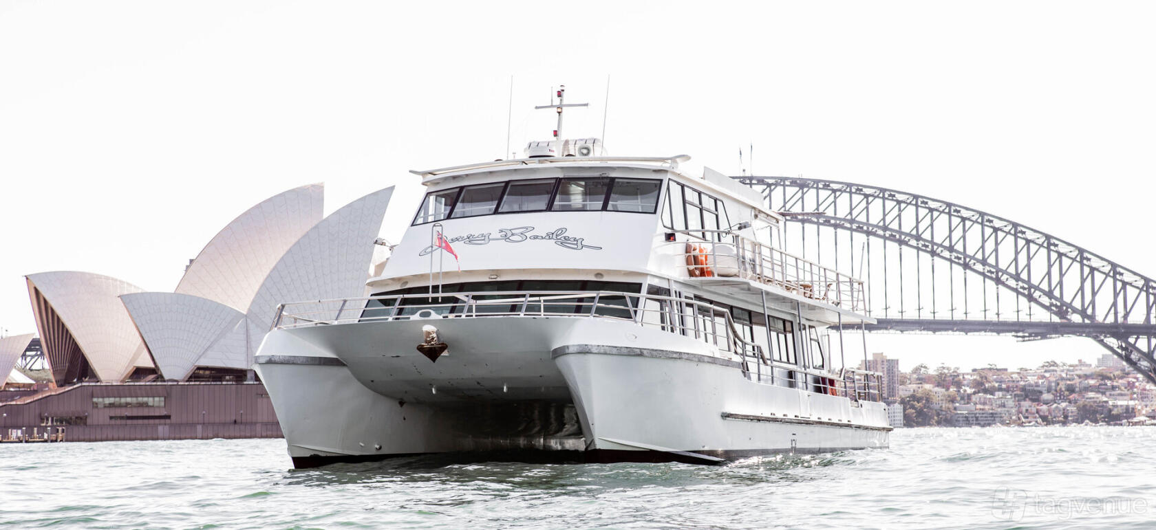 A charter boat with two decks and large windows, docked near the Sydney Harbour Bridge at MV Jerry Bailey.
