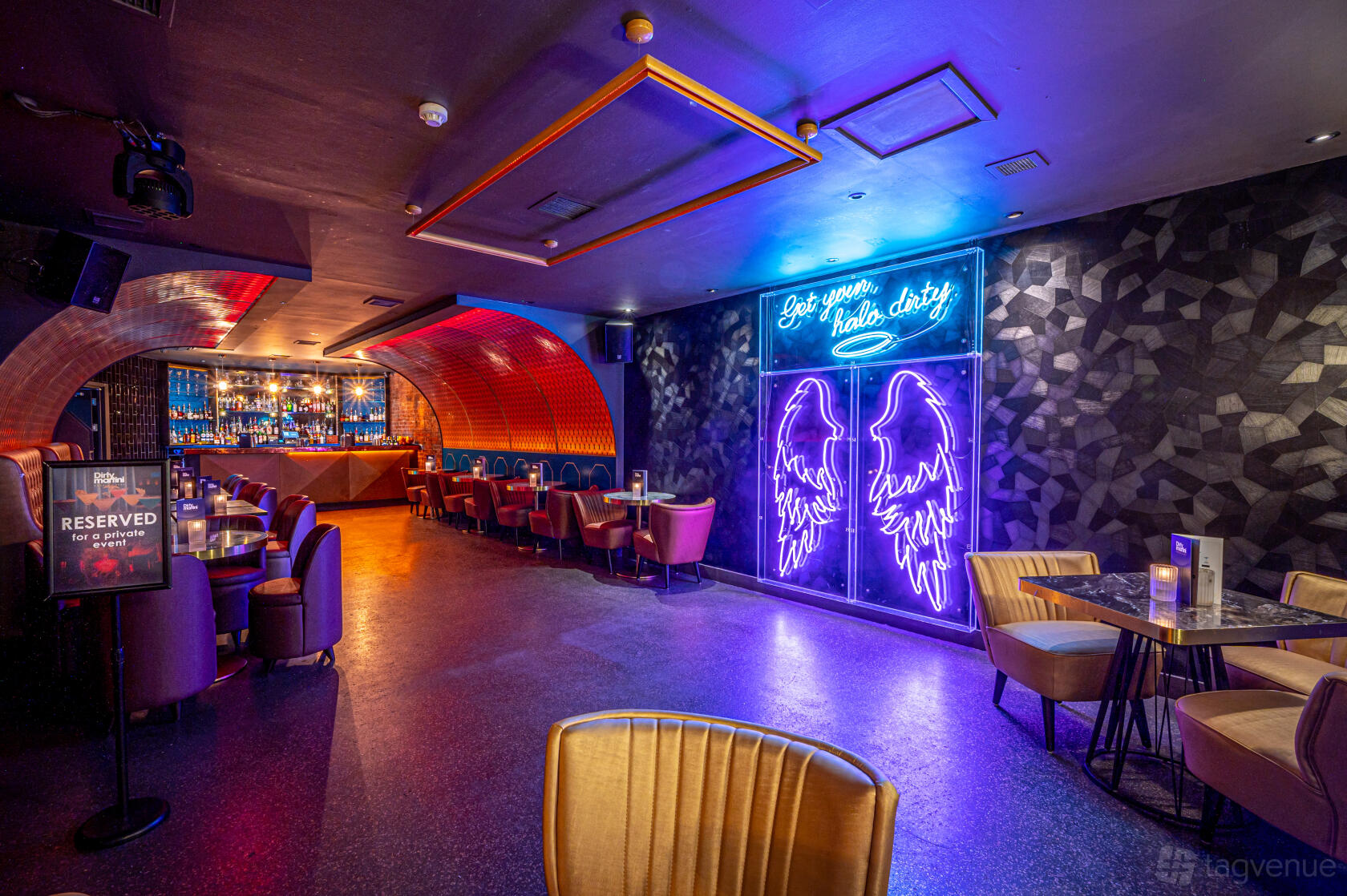 An event space in a cocktail bar with neon wall art, velvet seating, and a backlit bar at Dirty Martini Monument.