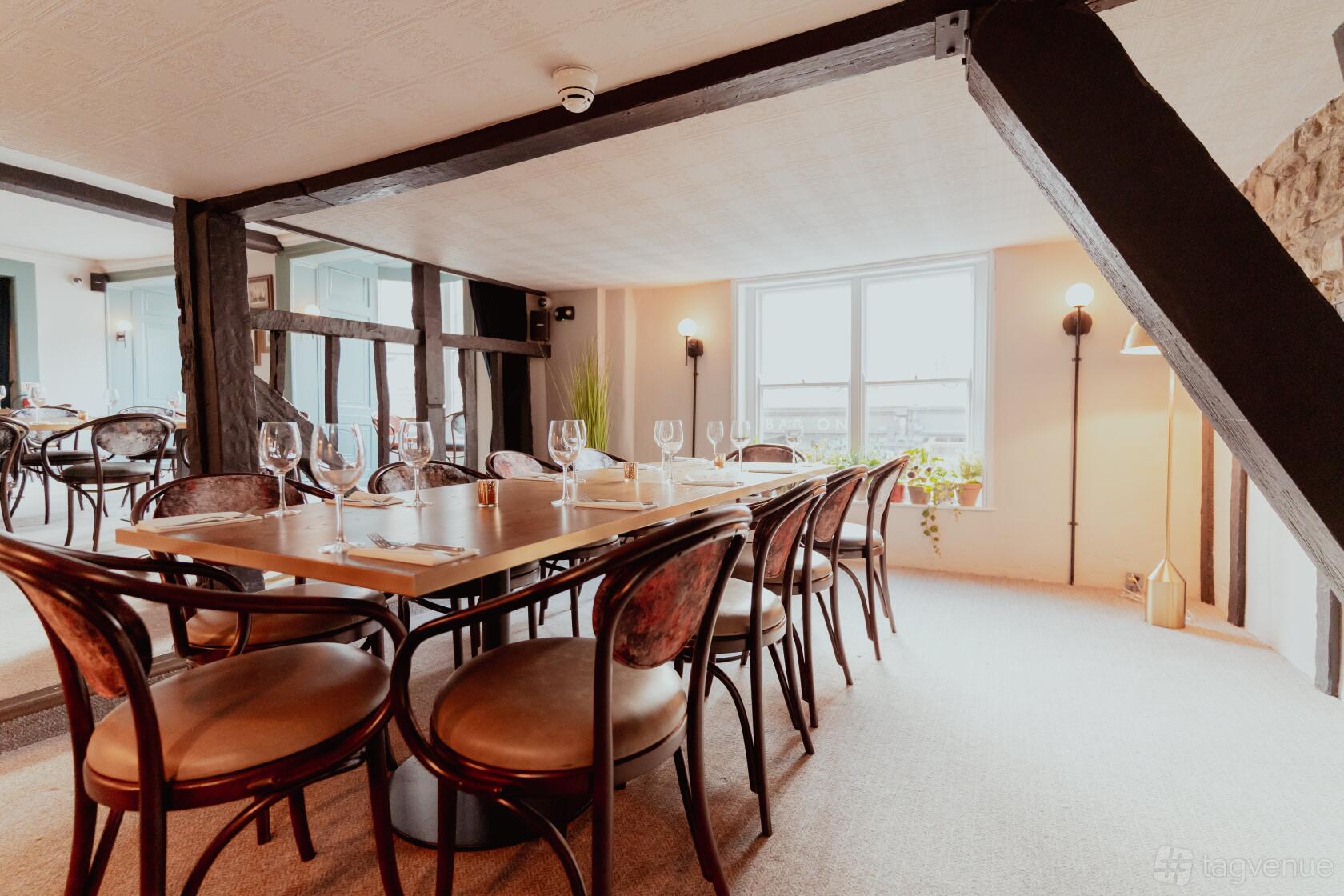 A dining room with wooden chairs, set tables, exposed beams, and large windows at Gusto Italian Oxford.