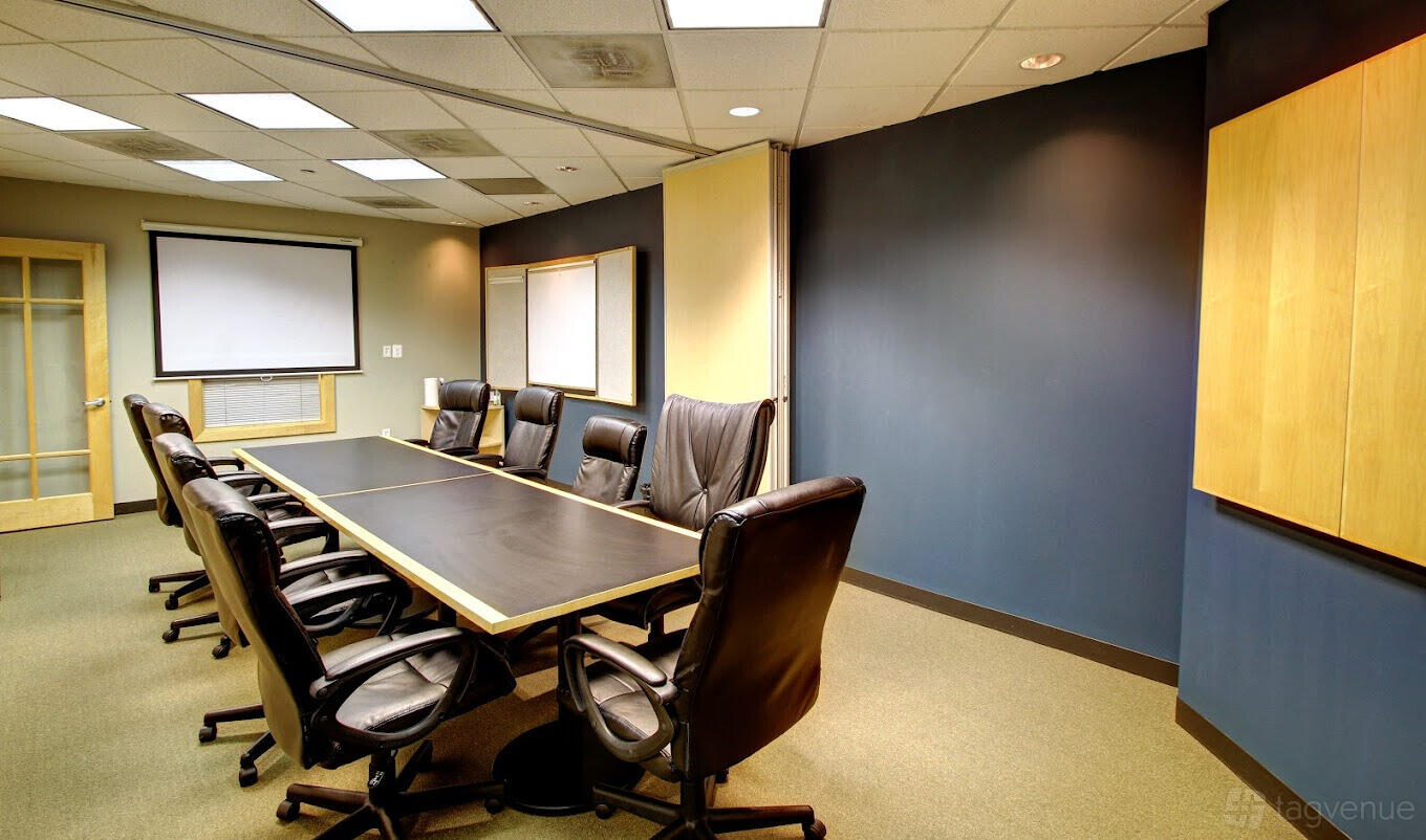 A meeting room with a long conference table, black leather chairs, and a wall-mounted projector screen at Intelligent Office.