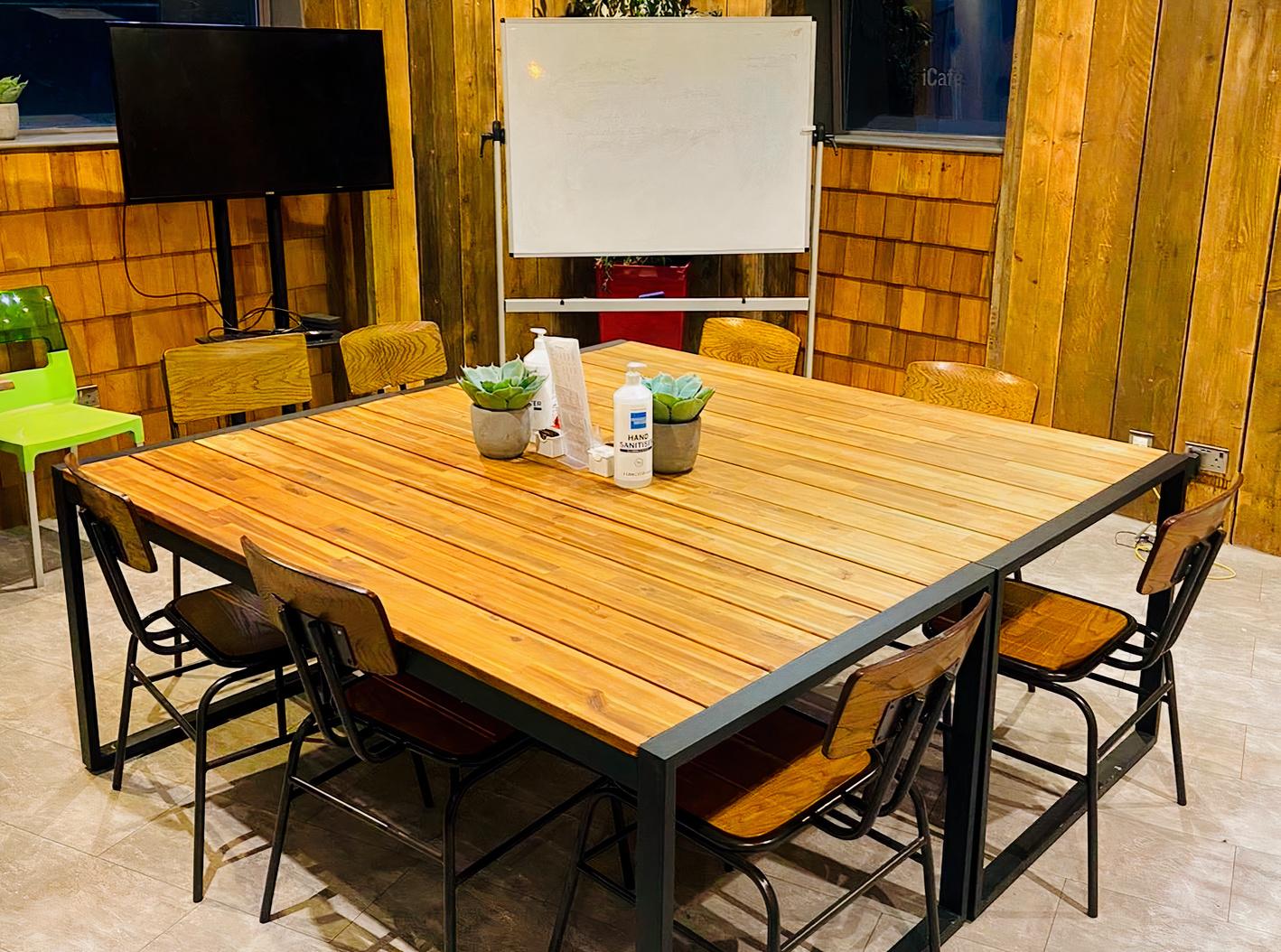 A meeting room with a wooden table, mixed chairs, potted plants, and a whiteboard at iCafe Merchant City.