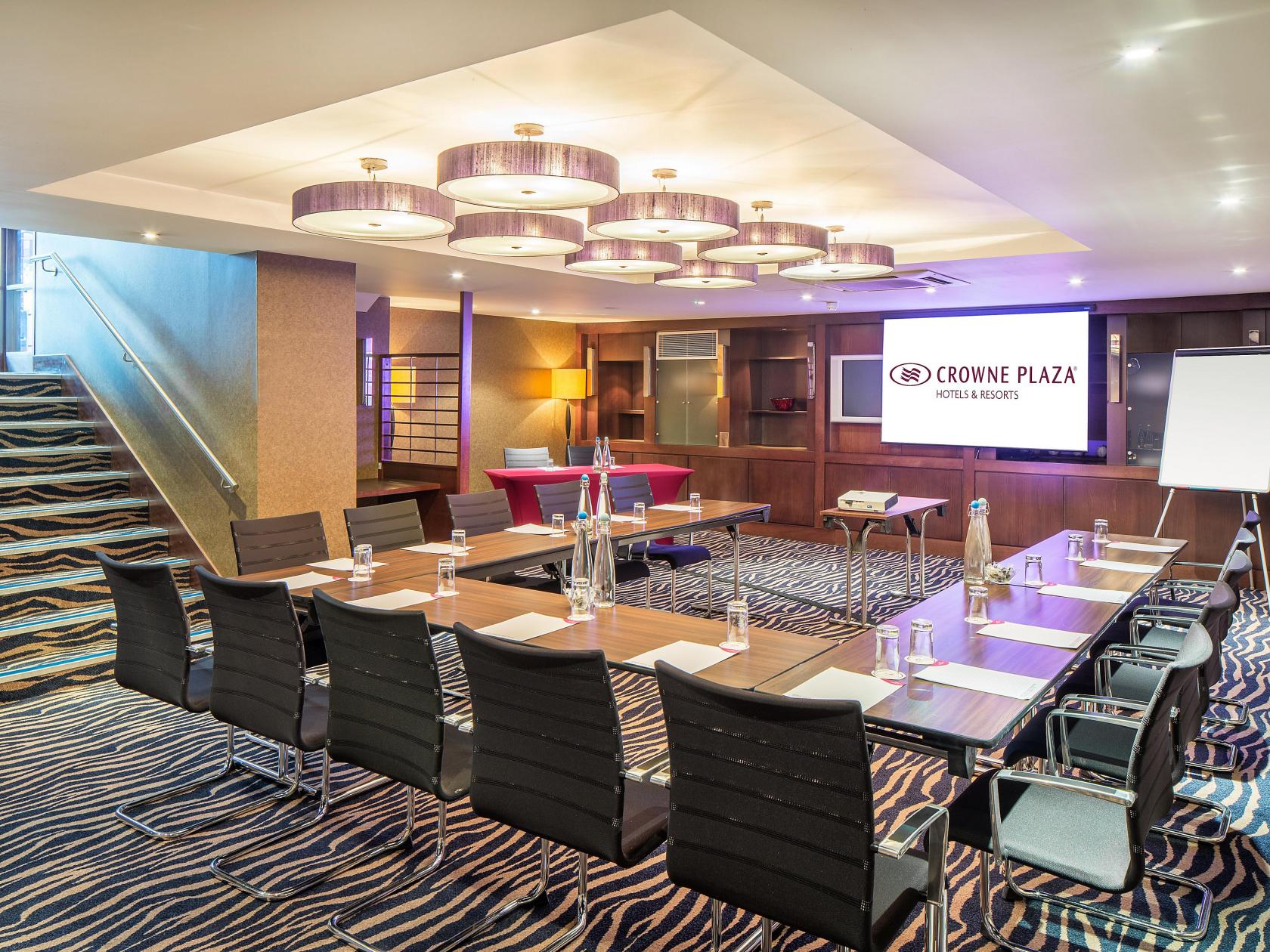 An event space with a long conference table, modern lighting, and patterned carpet at Crowne Plaza London Gatwick.