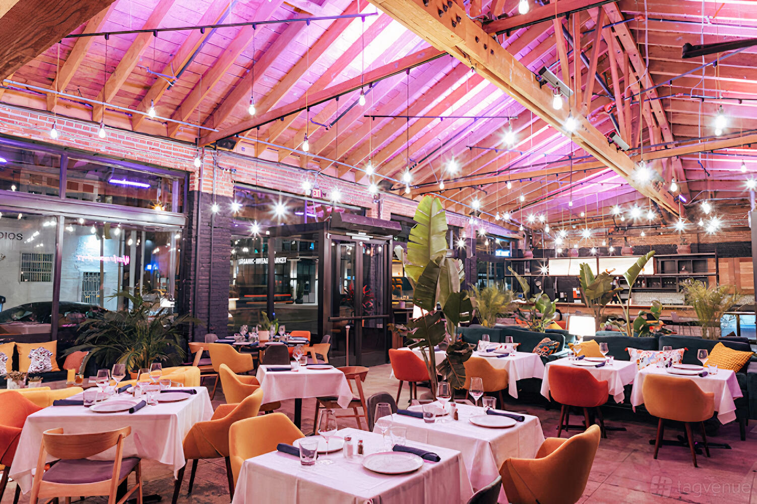 A restaurant with exposed wooden beams, string lights, colorful chairs, and white table linens at House of Cocotte.