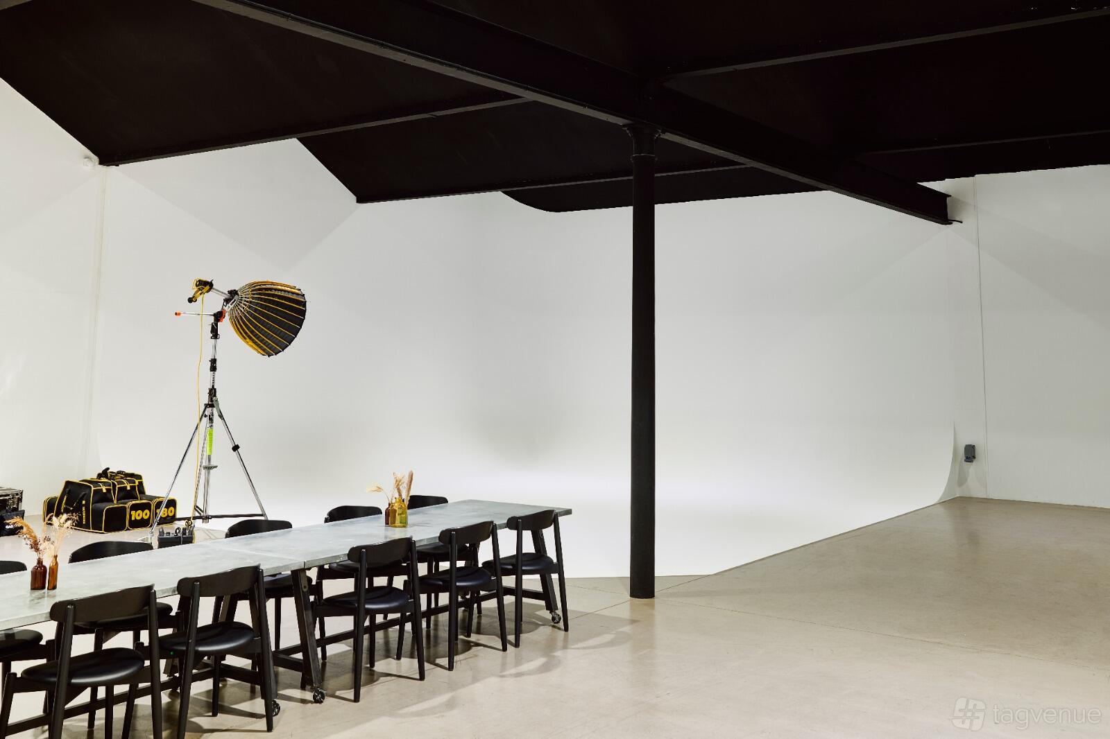 A photo studio with a white cyclorama wall, overhead black beams, and a table with black chairs at GAS Studios.